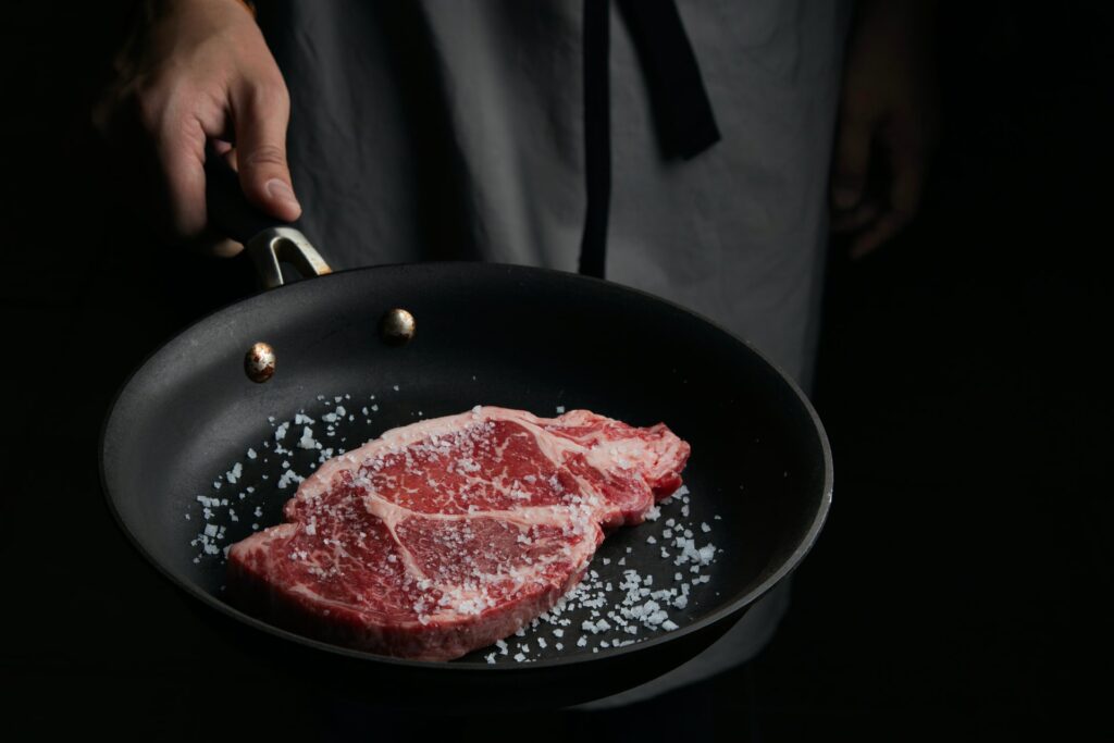 A well-marbled cut of steak in a pan, preparing to be seared. Learn why fat means flavor and how our Stanford's chefs treat lean vs. fatty steaks